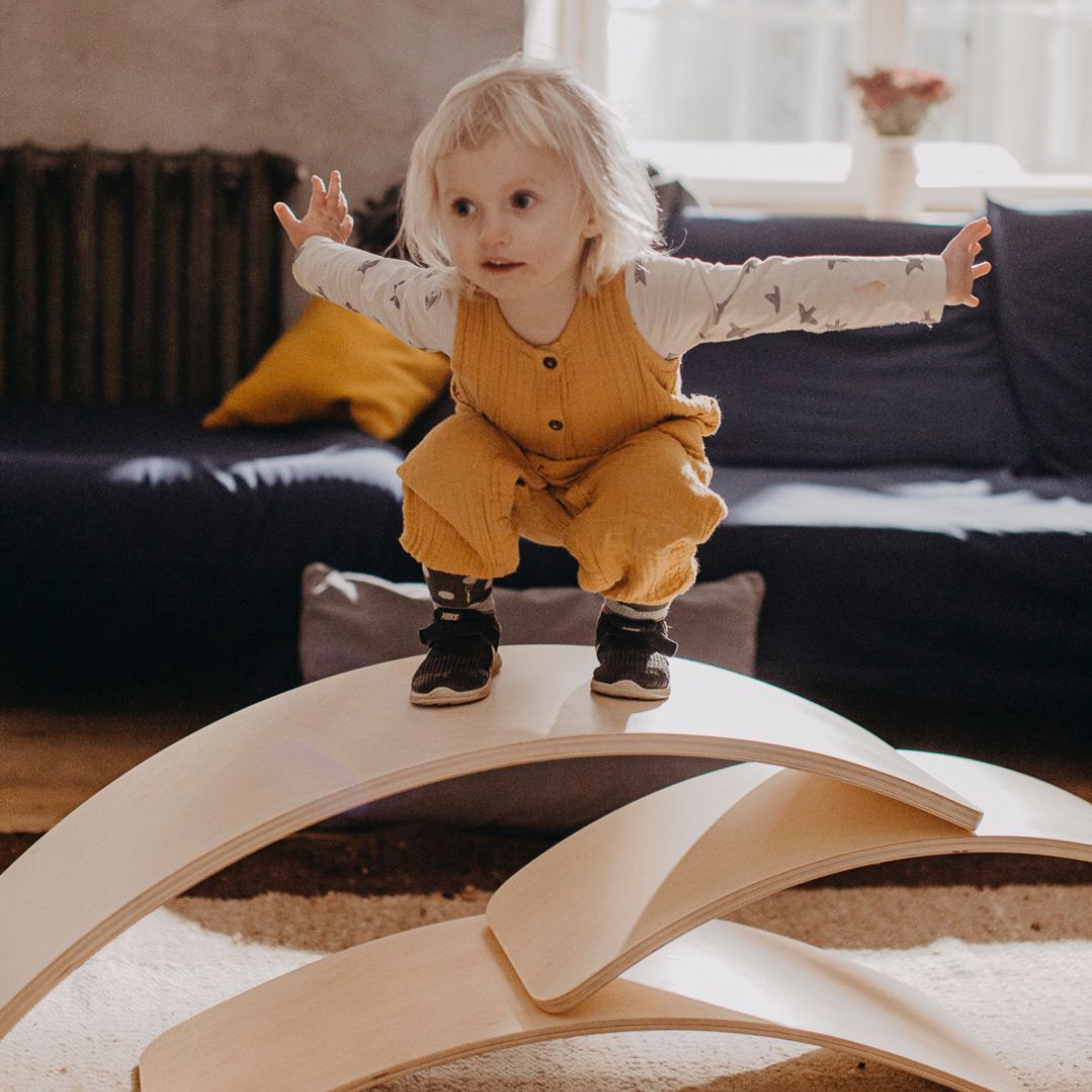 Child standing on three wooden balance boards arranged in an arch composition in the living room
