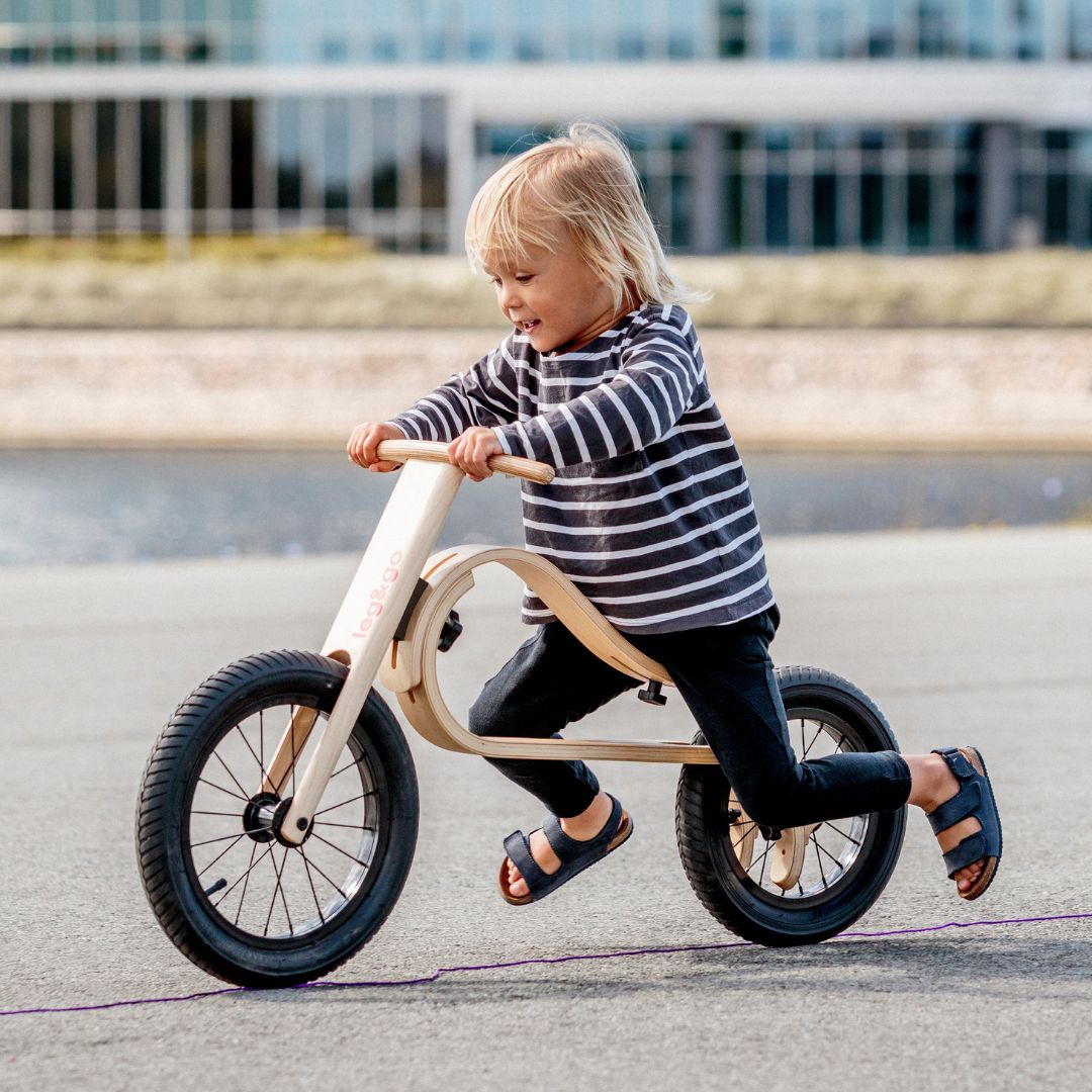 Child riding a wooden balance bike 3in1 on a road
