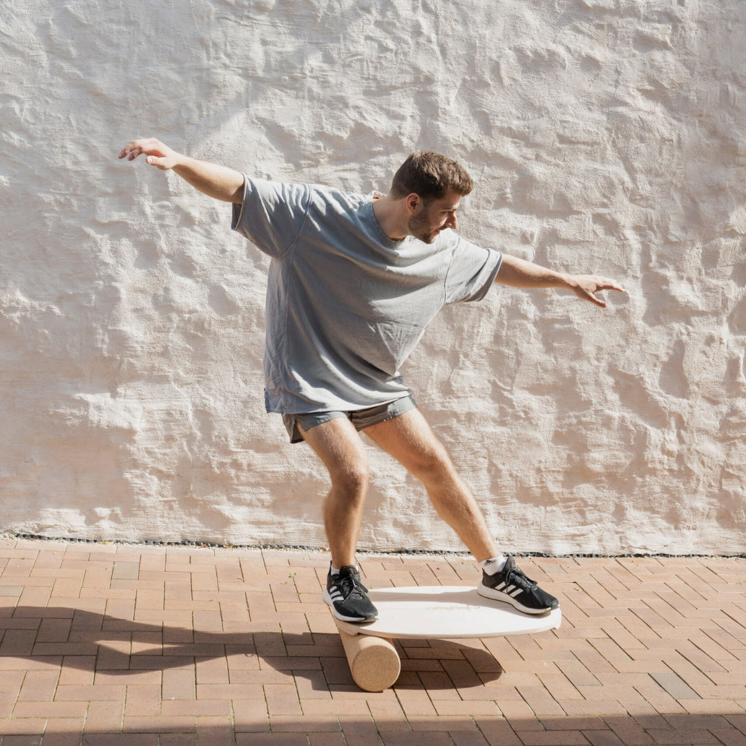 Man balancing on a wooden balance board with roller for core strength training