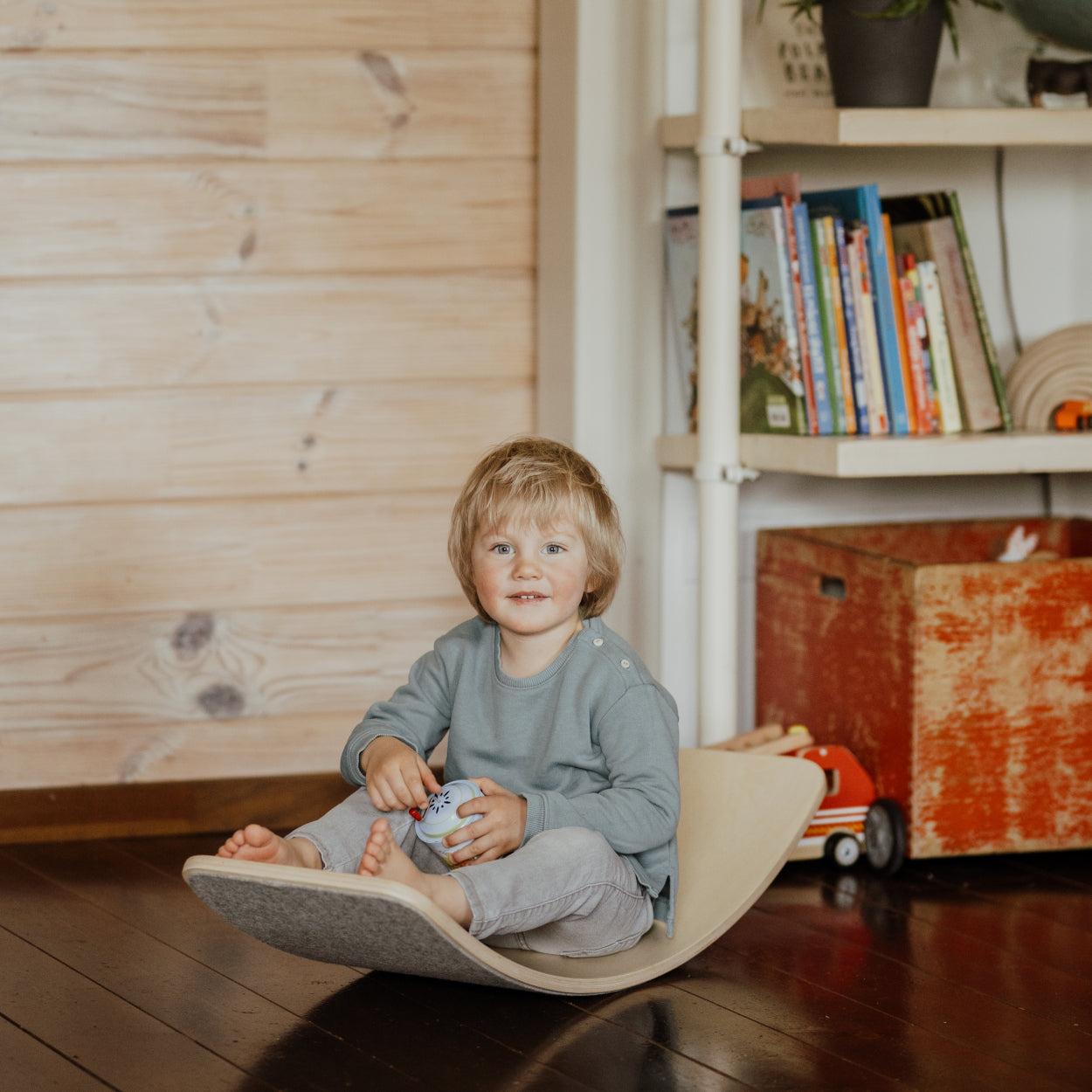 Boy sitting and swinging on the balance board as a rocking horse. 