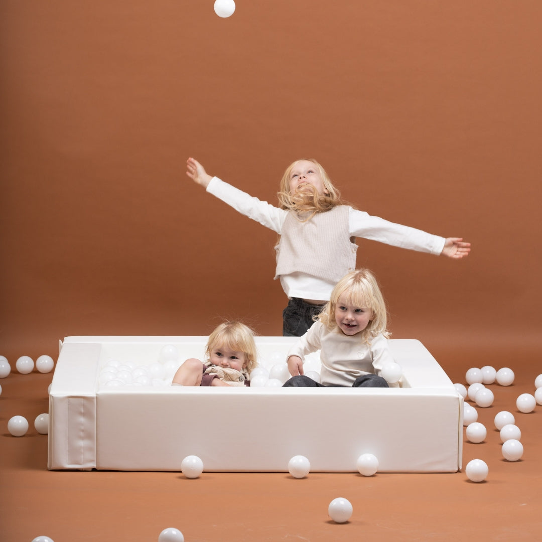 Children playing and interacting in a white soft play ball pit