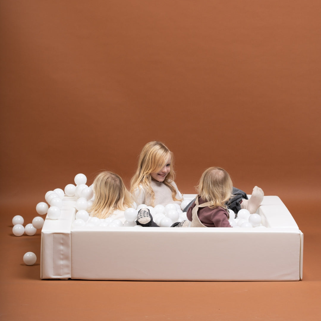 Three children sitting inside a white soft play ball pit
