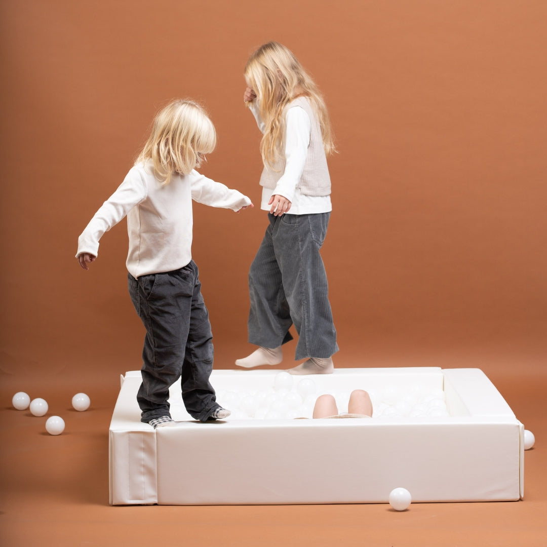Two children standing and playing inside a white soft play ball pit