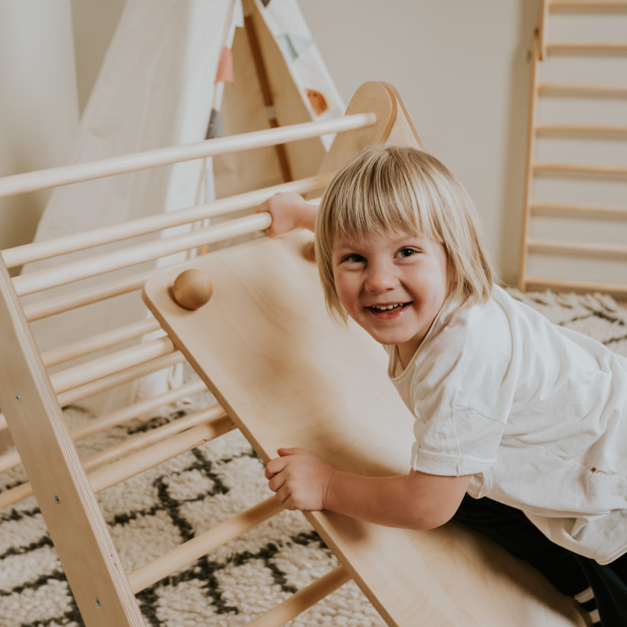 Child playing on top of ramp that is attached to wooden climbing triangle