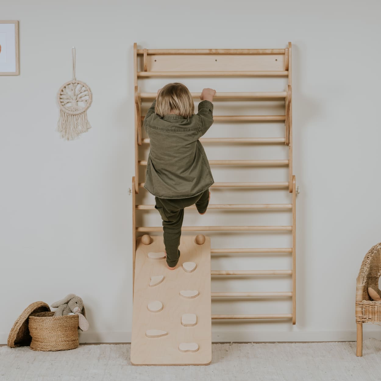 Child stepping on a ramp that is attached to Swedish ladder wall set in natural wood color