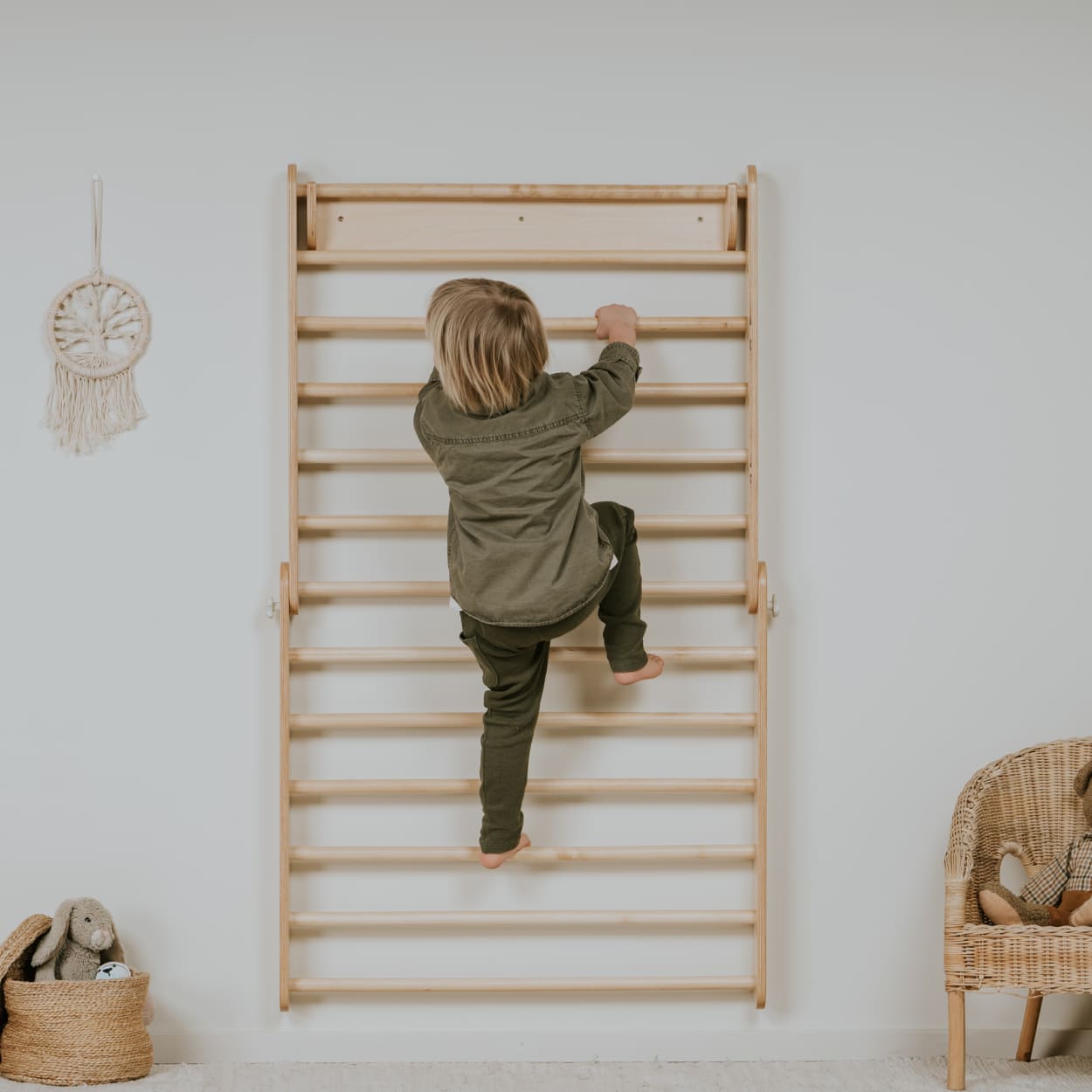 Child climbing a wooden Swedish ladder on a white wall with minimal decor.