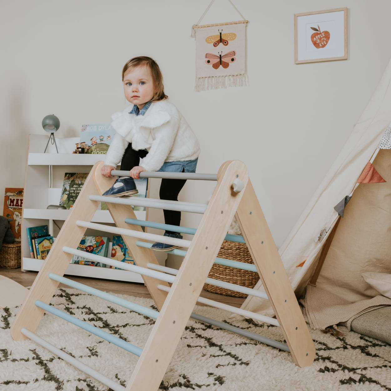 Girl climbing over wooden play gym triangle.