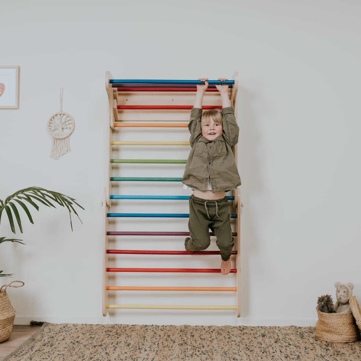 Child hanging on colorful Swedish ladder top bar.