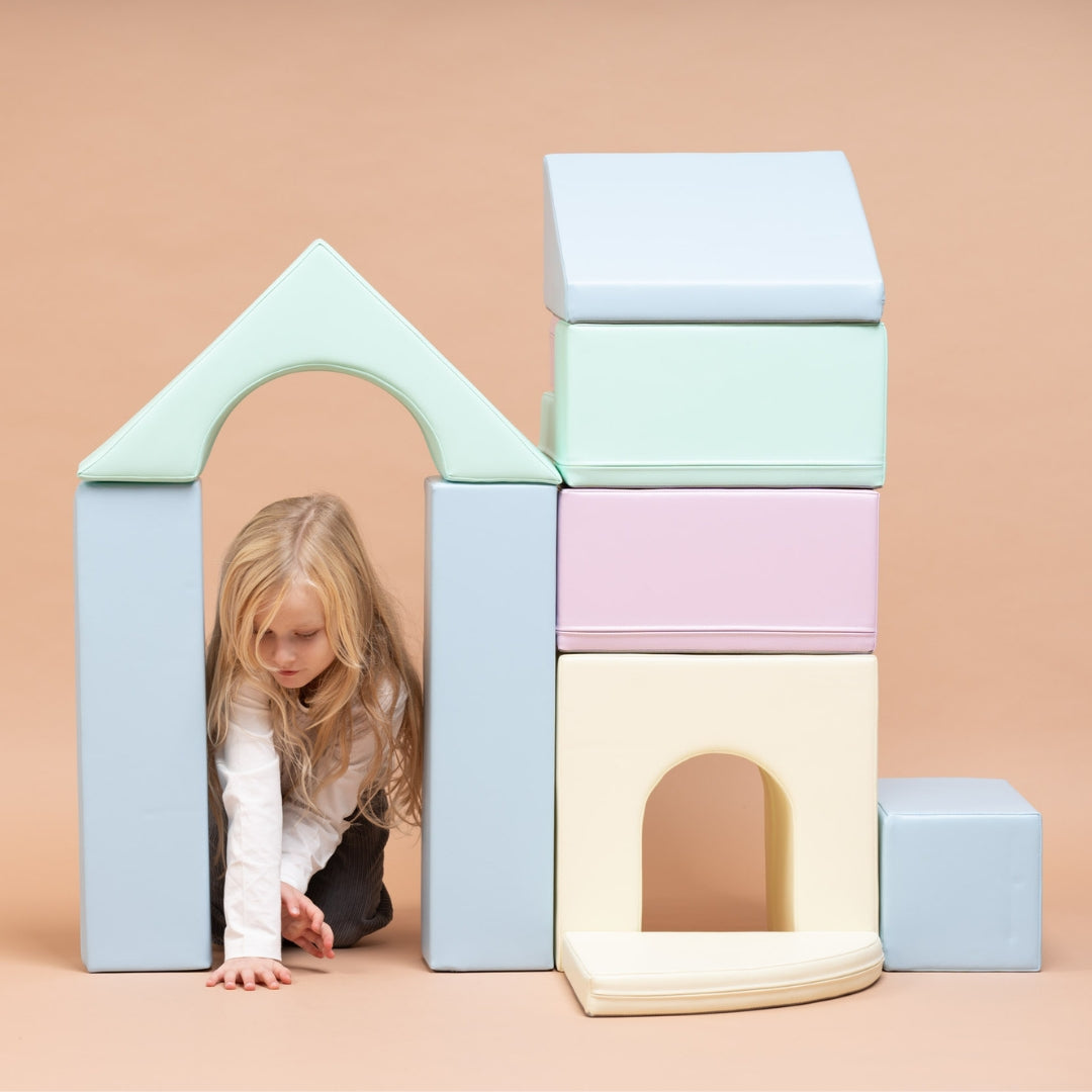 Child crawling underneath a bridge-like structure built from light pastel Creativity soft play blocks