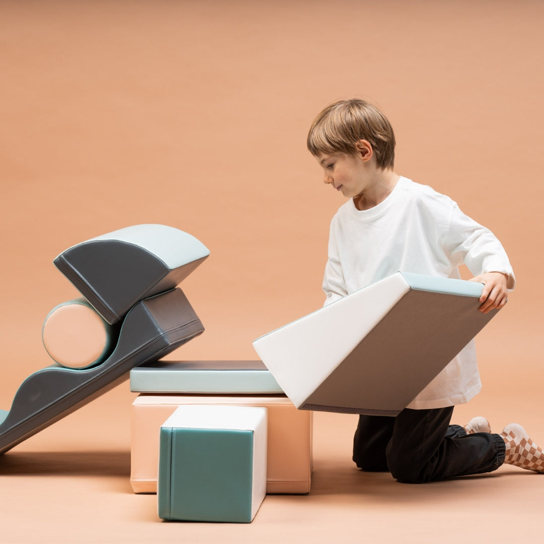 Child playing with Discoverer soft play blocks in light pastel tones, exploring and lifting a foam block
