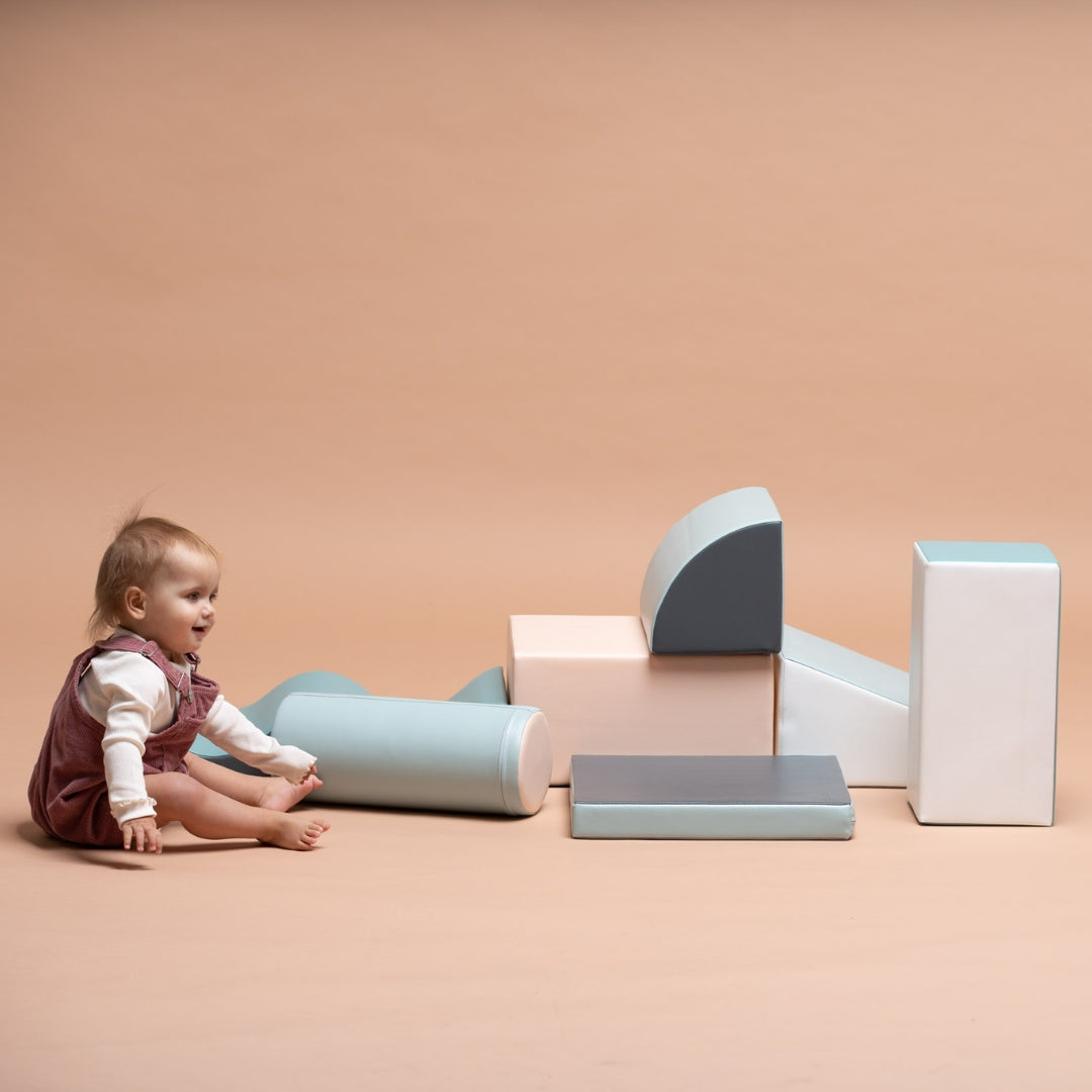 Child sitting on floor with light pastel Discoverer set blocks scattered around for open-ended play