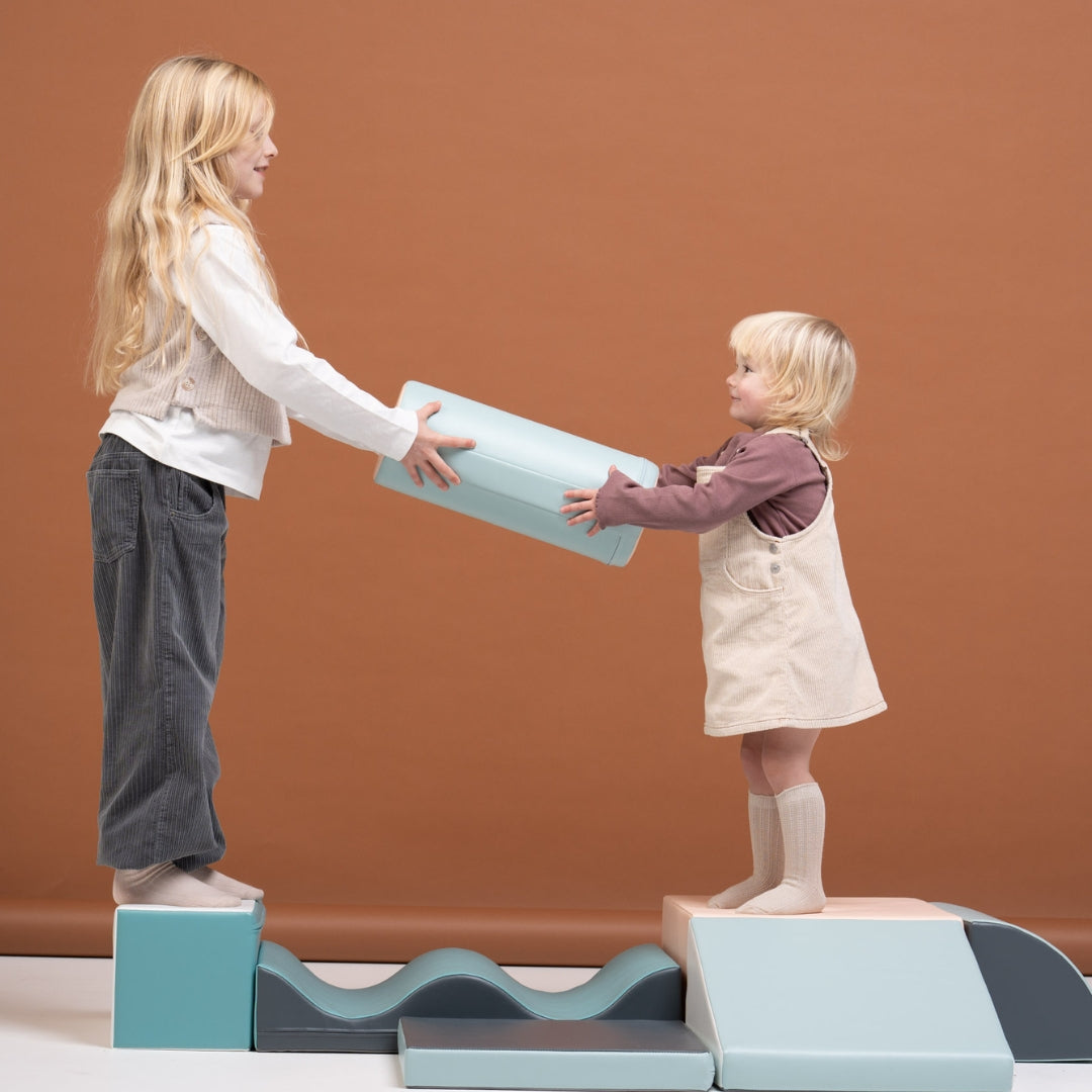 Two children interacting with pastel-colored Discoverer soft blocks, stacking and handing each other pieces