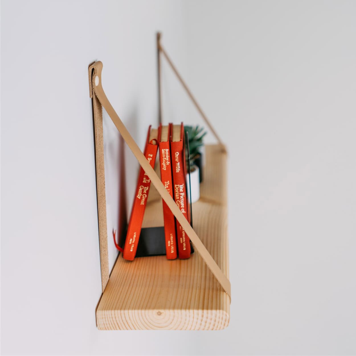 wooden floating shelf with leather straps as mounting choice.