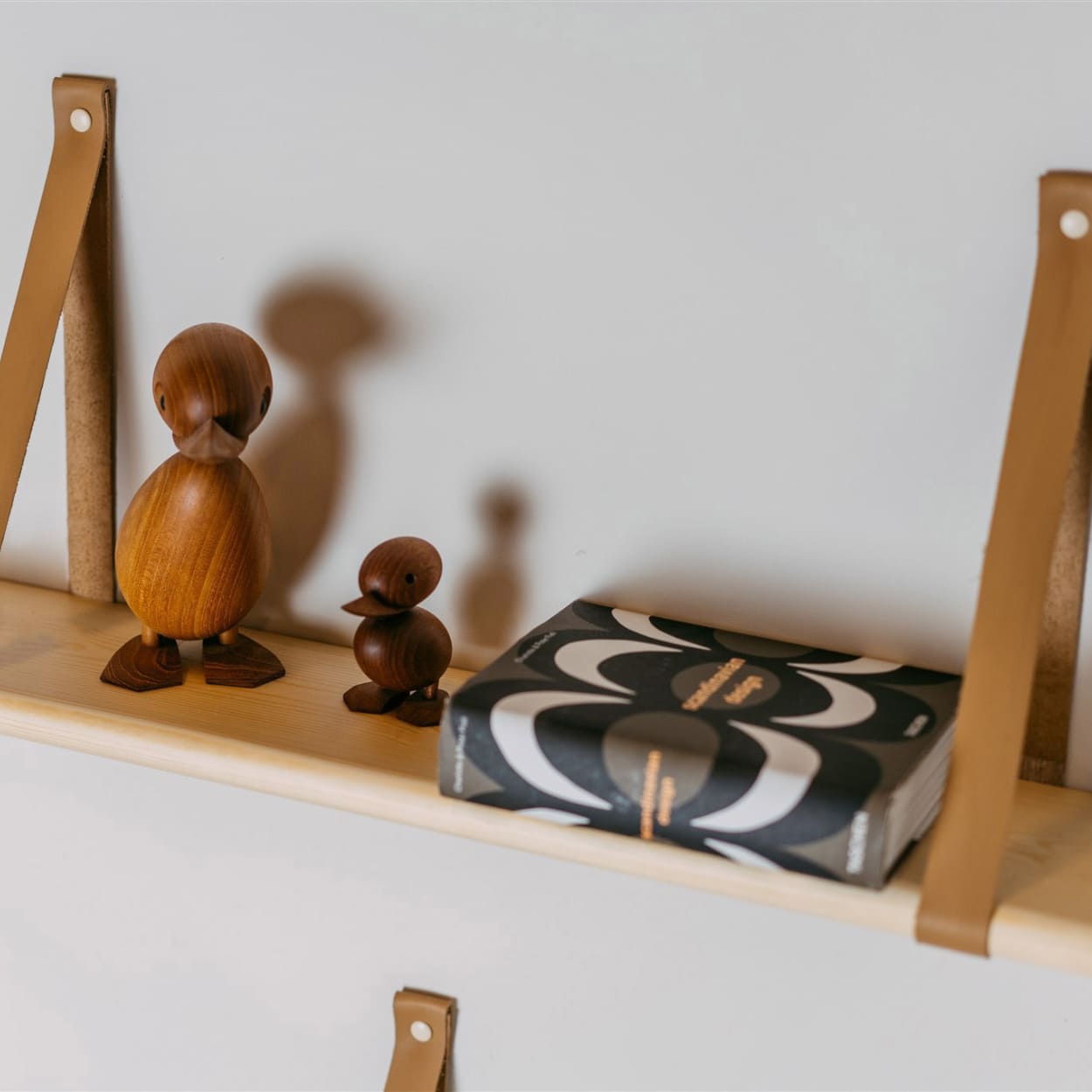 Accessories stacked on pine wood floating shelf with leather straps