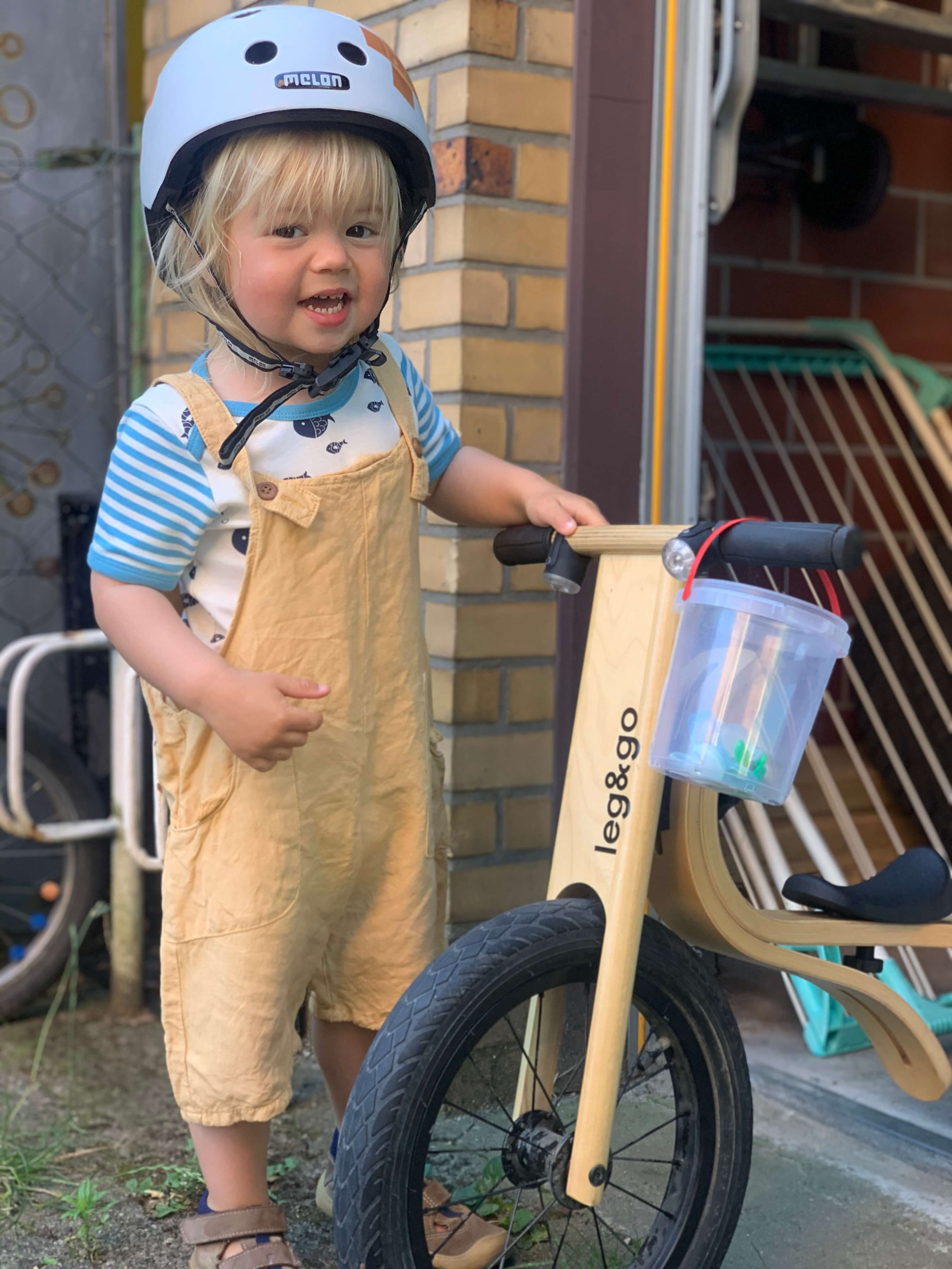 Child standing next to a wooden 3-in-1 leg&go balance bike outdoors
