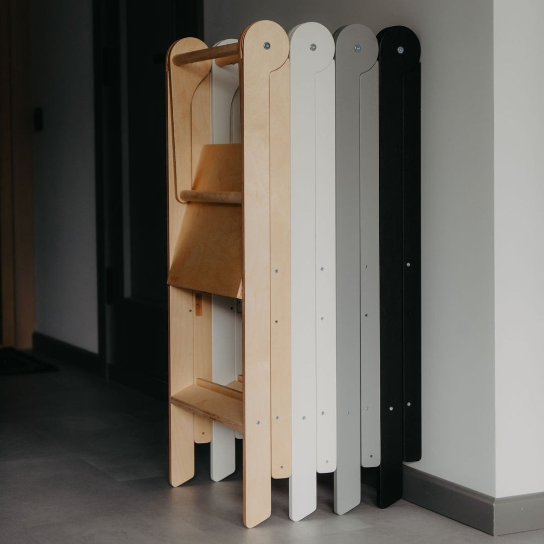 Set of four kitchen helper towers in different colors, folded and leaned against a neutral wall, showcasing a space-saving design