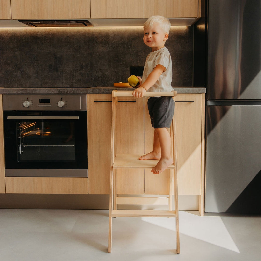 Child enjoys a snack on Leg&Go Foldable Helper Tower Natural at kitchen counter