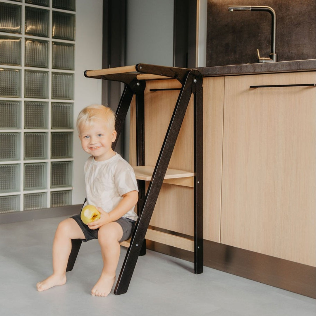 Toddler eating an apple while sitting on Leg&Go Foldable Helper Tower Black