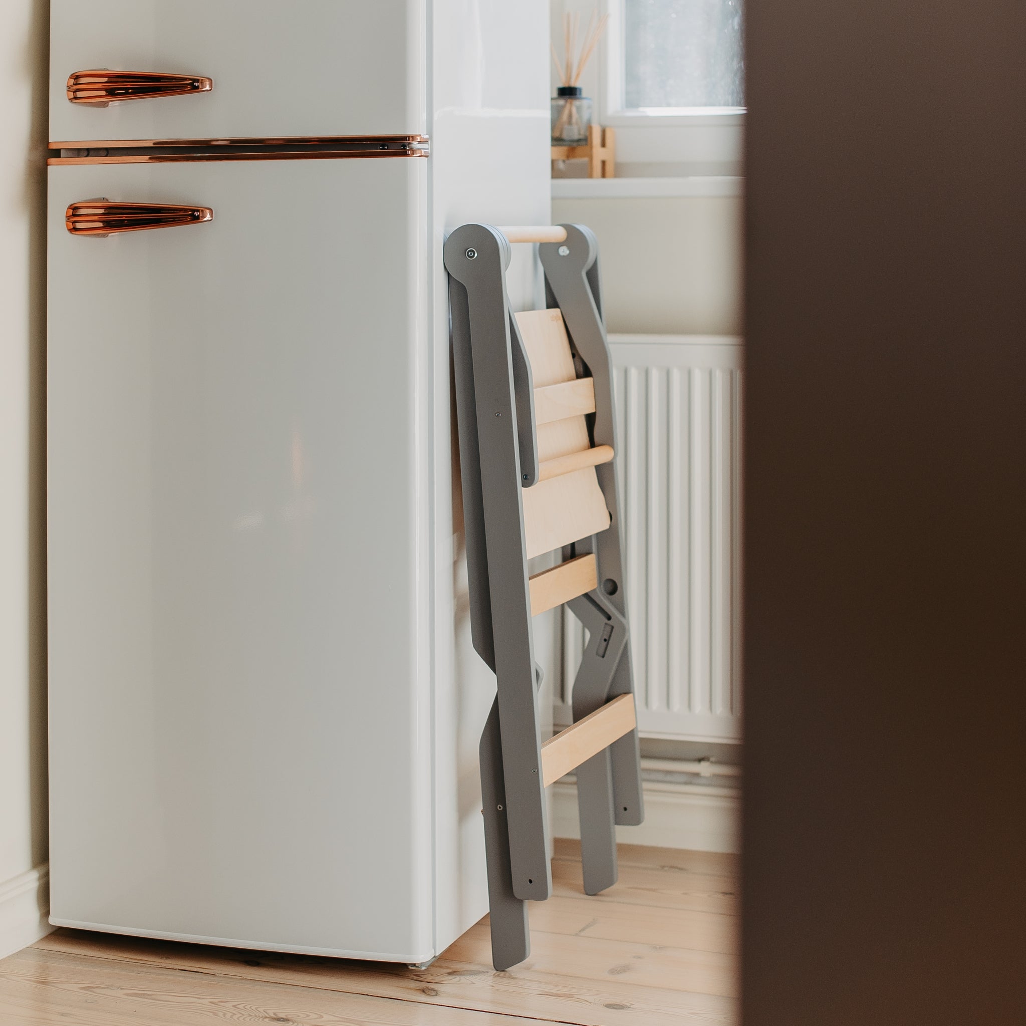 compact foldable learning tower stored beside fridge