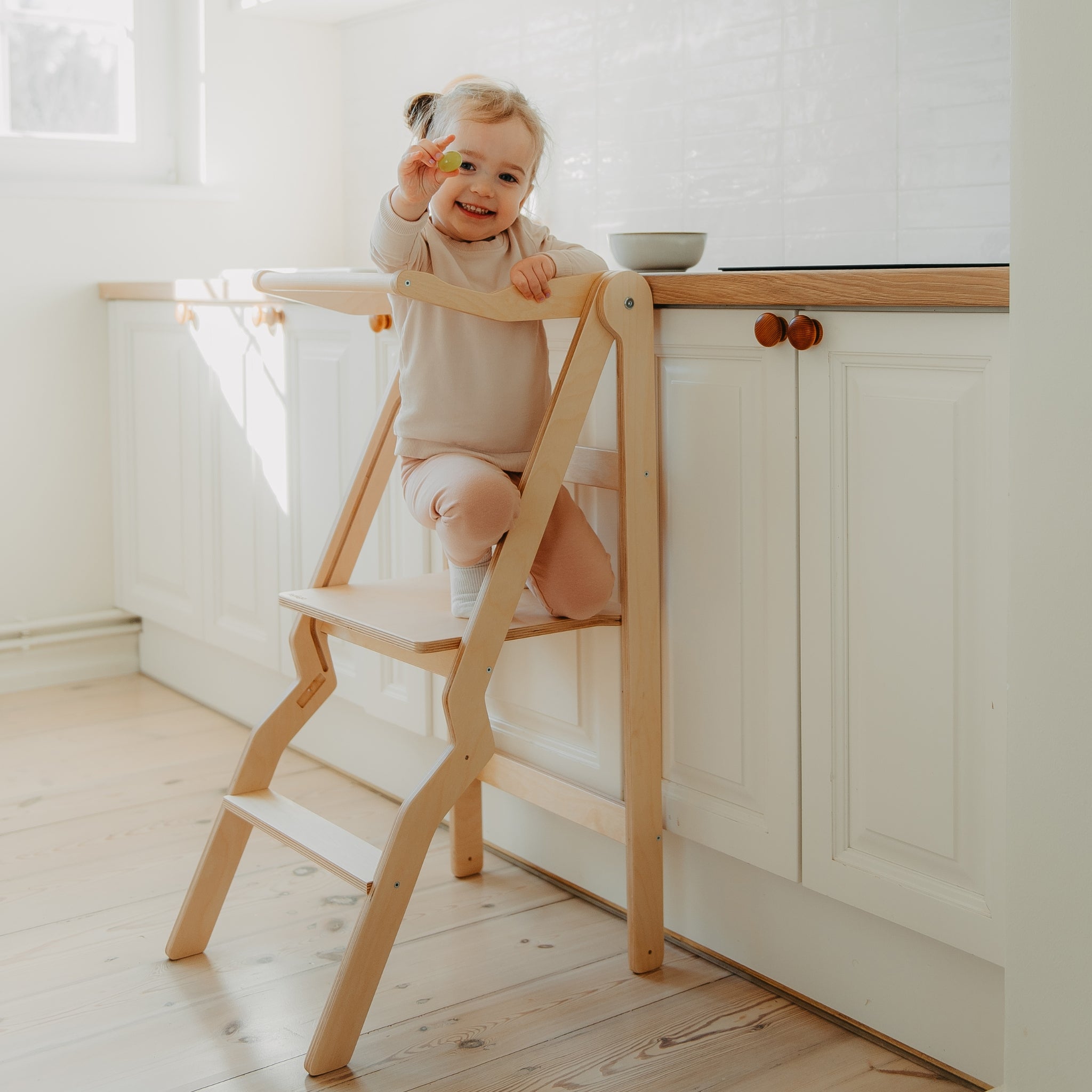 toddler using natural wood foldable learning tower in kitchen