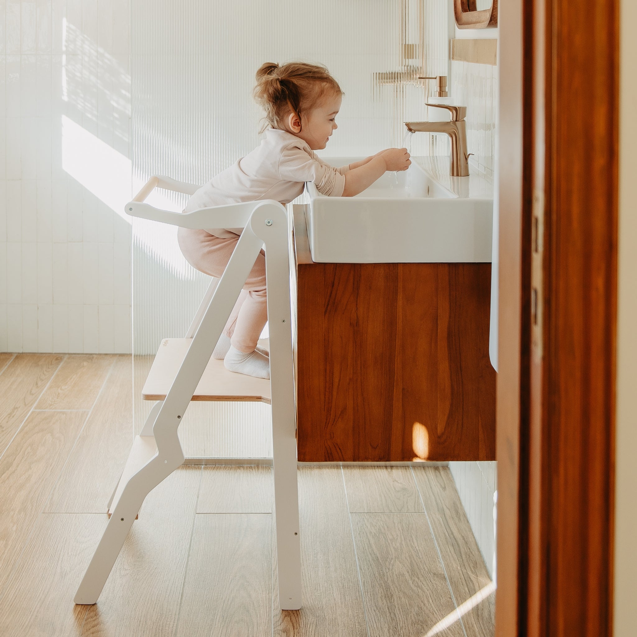 white wooden helper tower for toddlers standing at kitchen counter