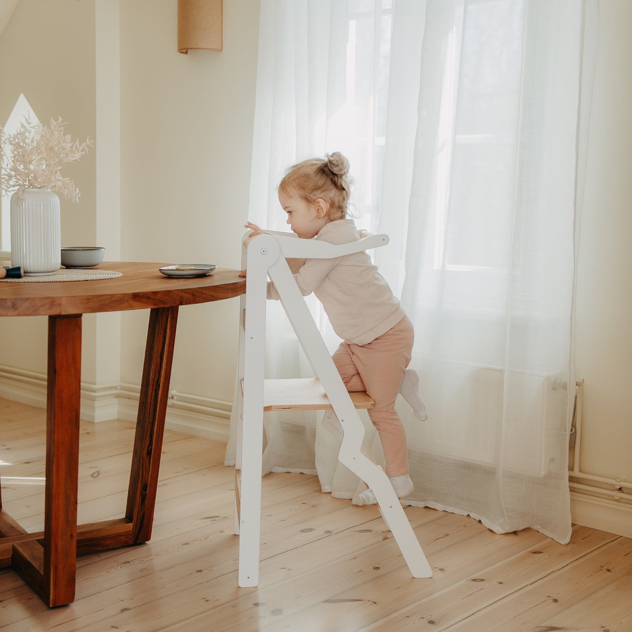 toddler using white foldable kitchen tower with safety rail