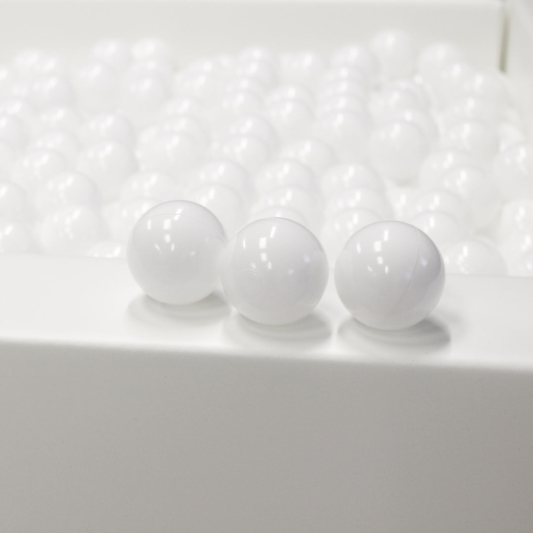 Three white balls in front with a ball pit full of balls in the background
