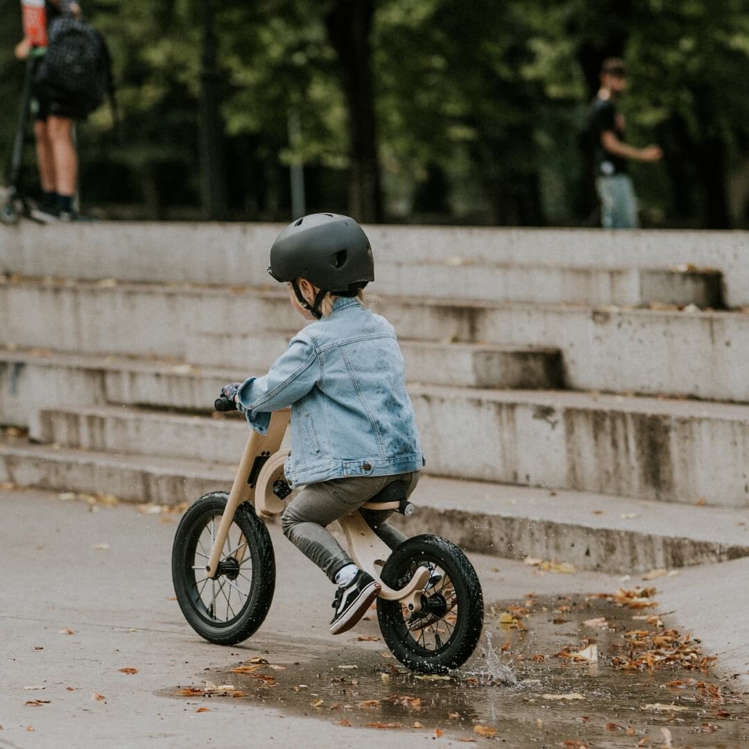 Child riding a balance bike on a wet pavement wearing black helmet