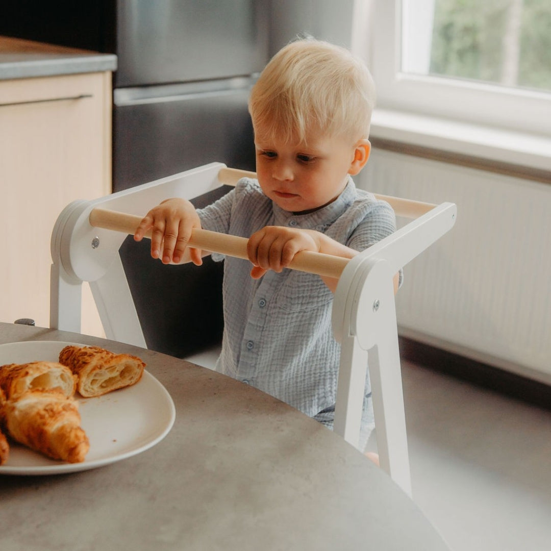 Child standing on a white kitchen tower at the kitchen table