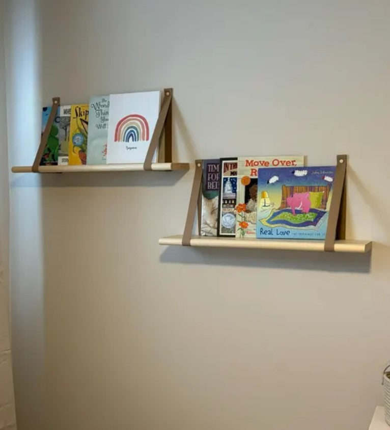 Wooden wall shelves with brown leather straps on a plain wall