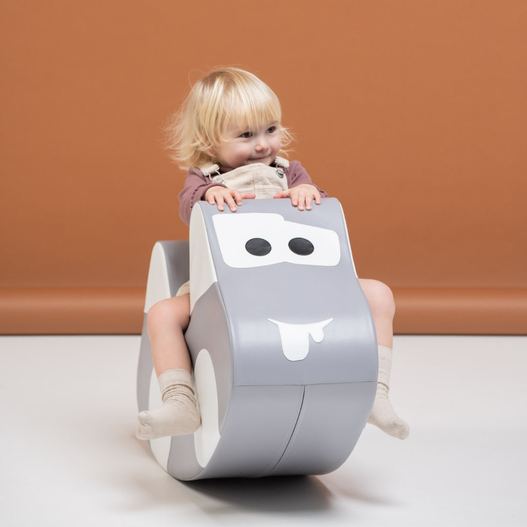Child leaning forward on gray rocker car toy, enjoying active soft play session