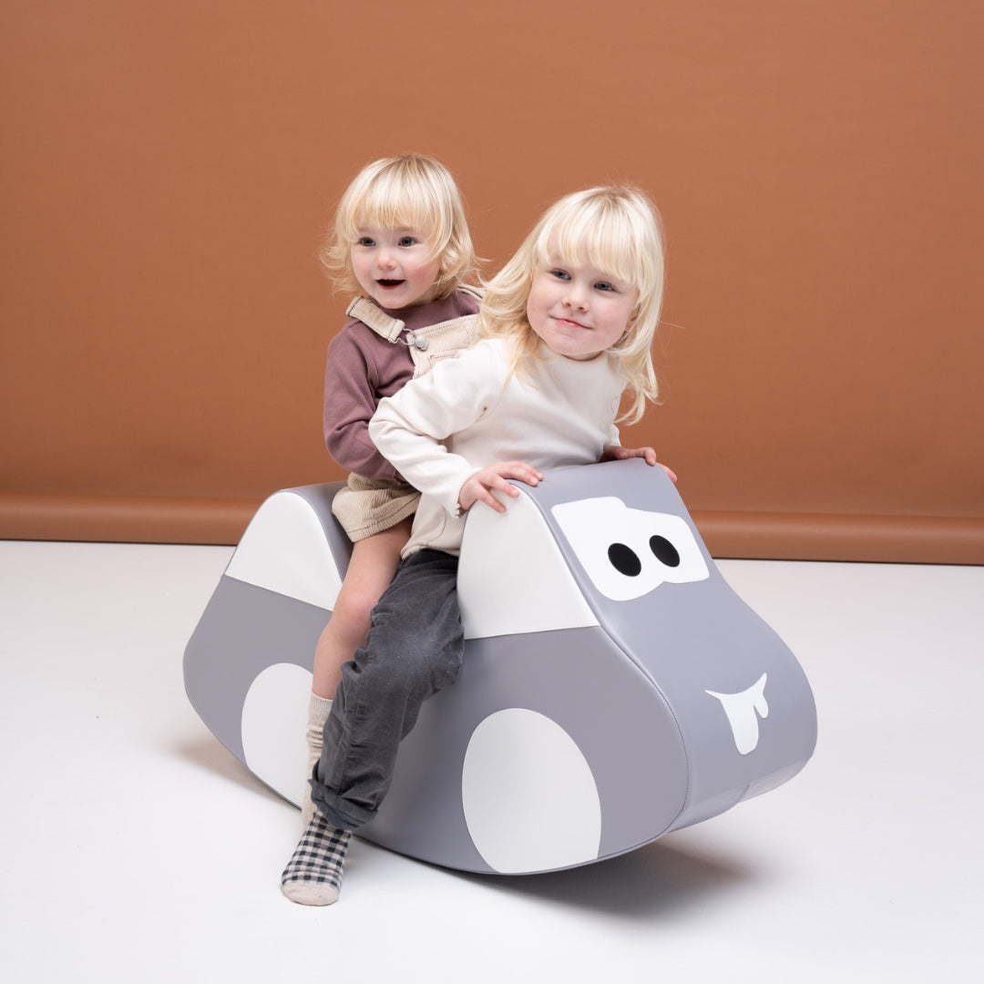 Two children playing together on gray soft play rocker car, promoting social and motor skills