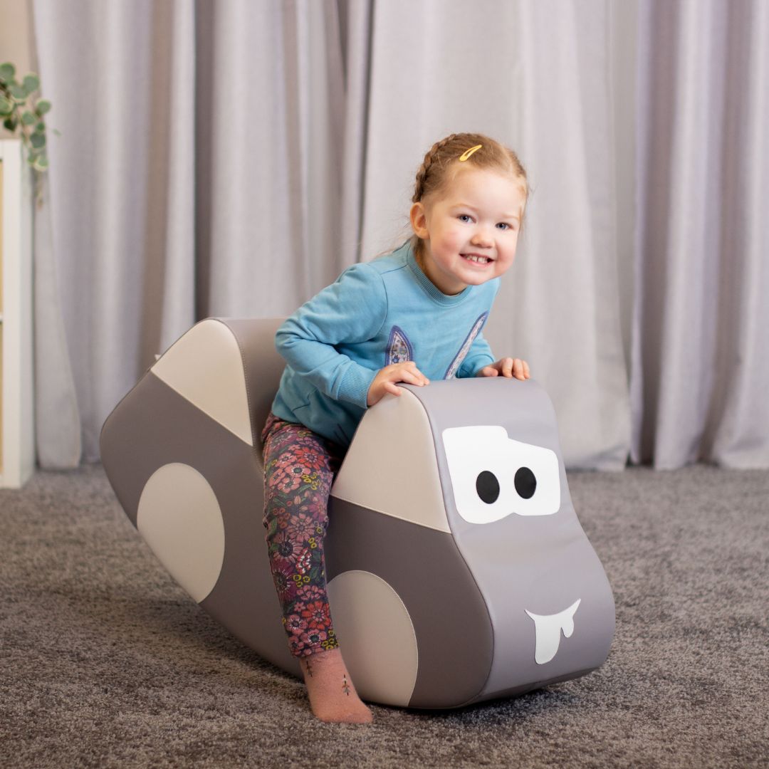 Smiling child playing on gray ride-on rocker car toy, enjoying active movement and fun