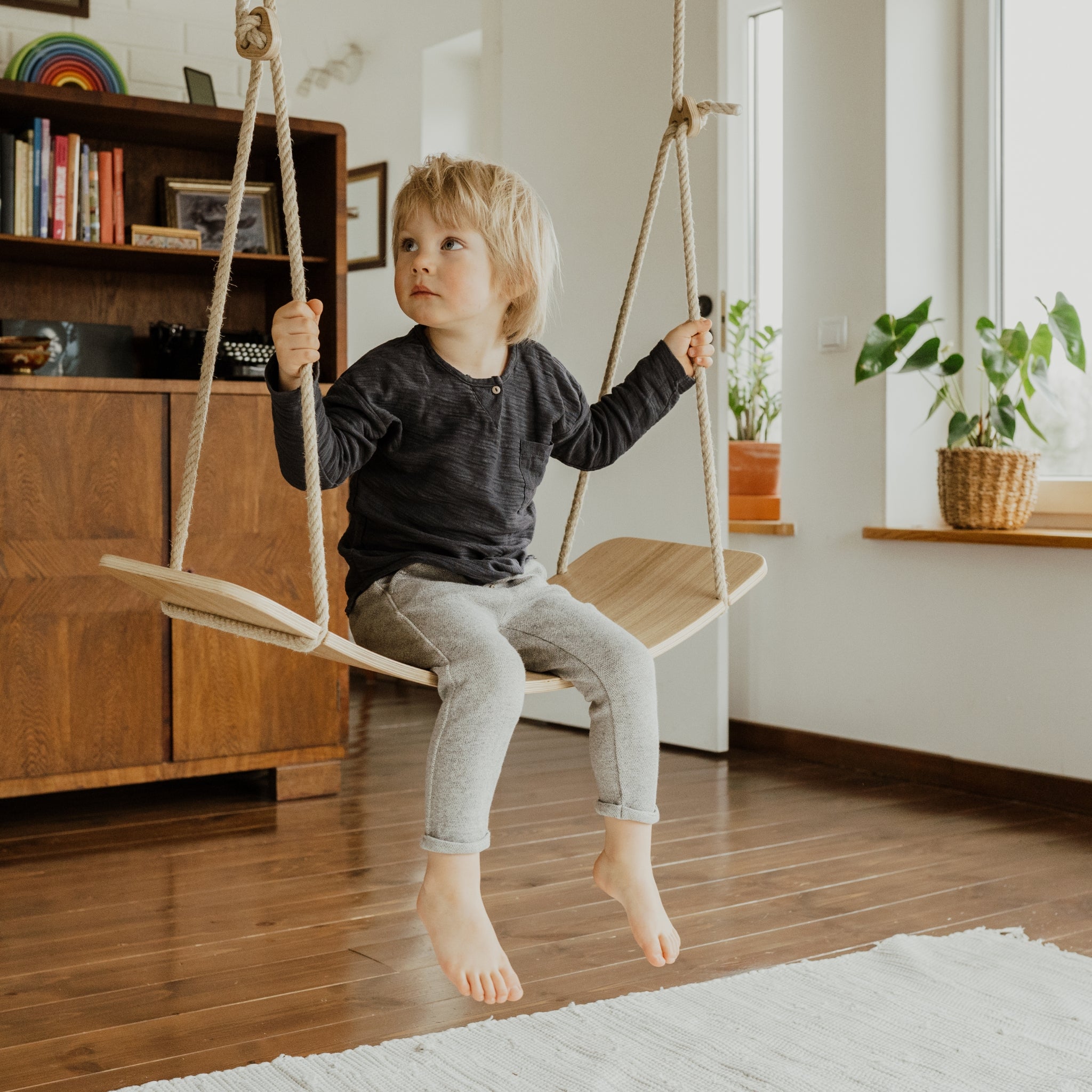 Child using indoor wooden wooden swing board at home