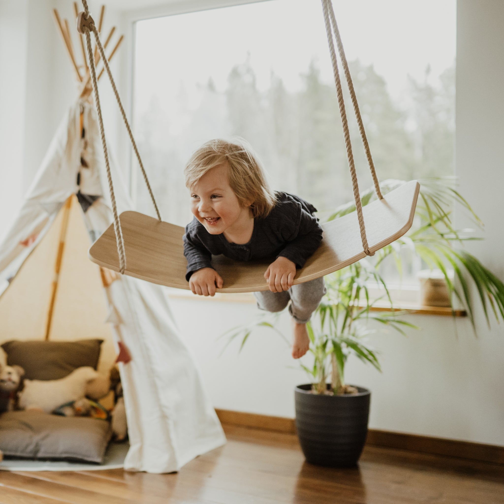 Happy child using indoor wooden swing board at home