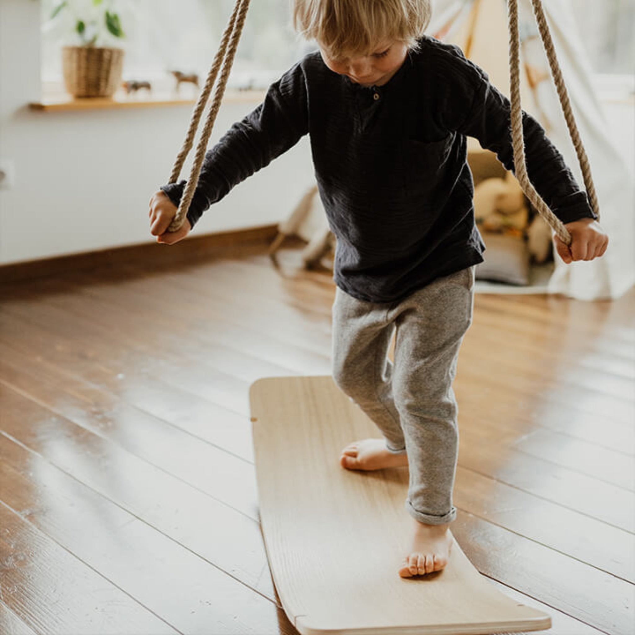 Kid balancing on wooden wobble board indoors