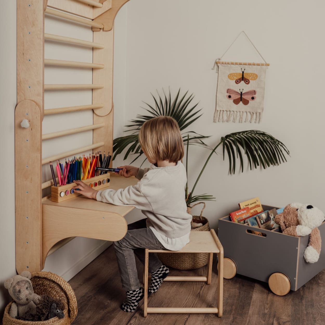 Child sitting next to a wooden desk that's a part from swedish ladder climber set add on