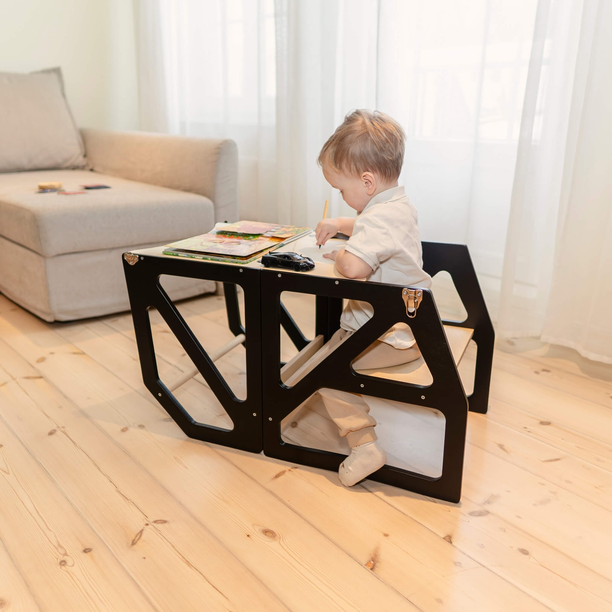 Child using black adjustable kitchen tower in table and chair mode