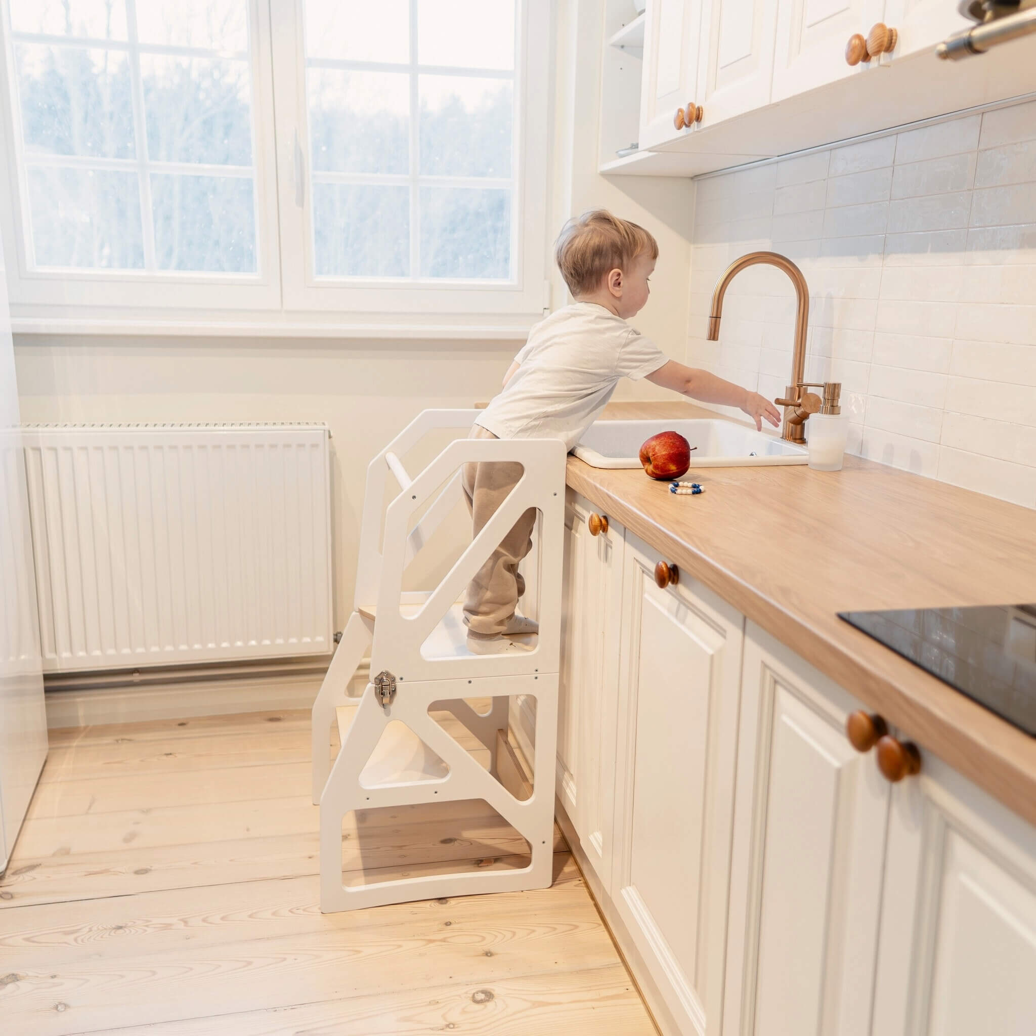 Child using transformable kitchen tower as adjustable step stool at kitchen counter