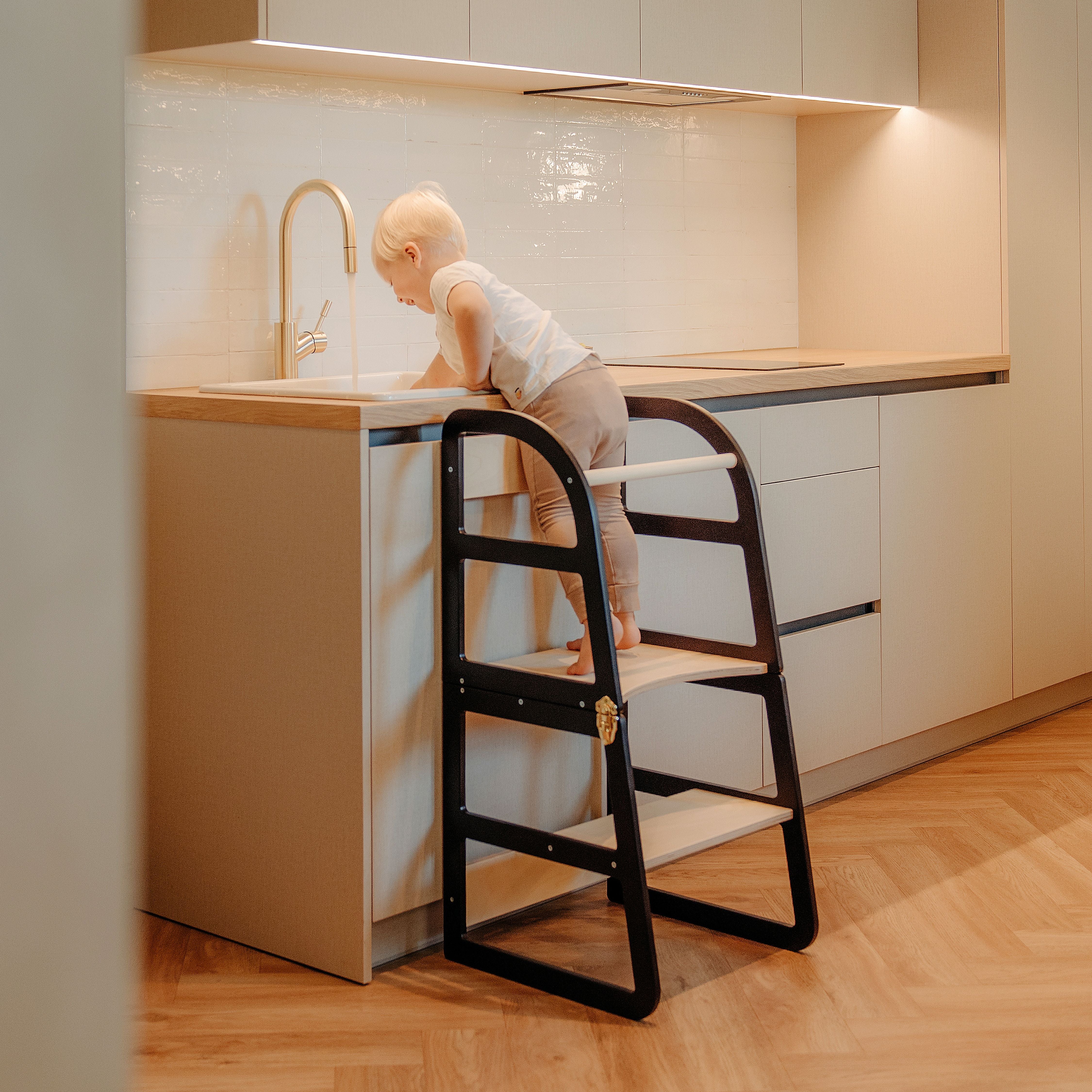 Child standing on transformable kitchen tower black color to help with kitchen tasks