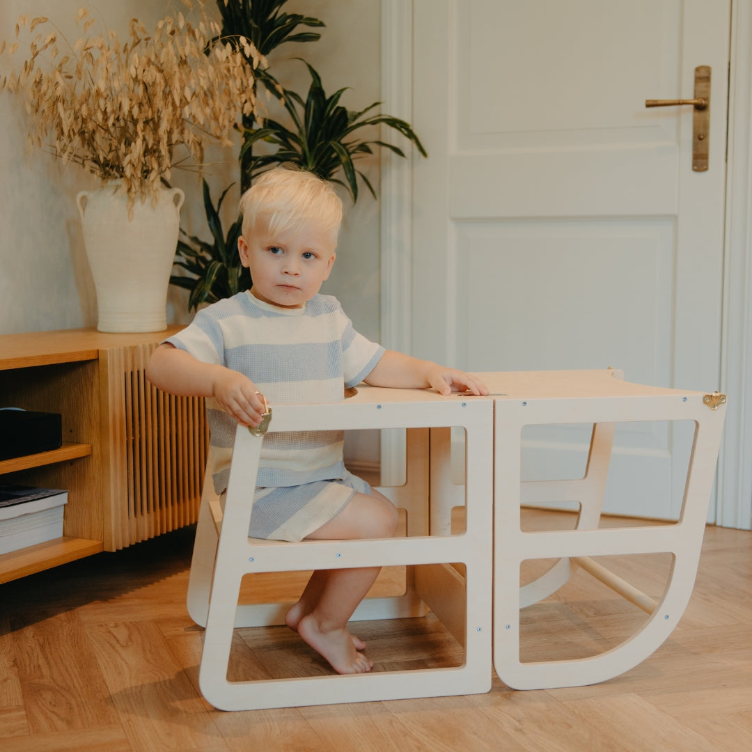 Child using a transformable kitchen tower converted into a table and chair for independent play