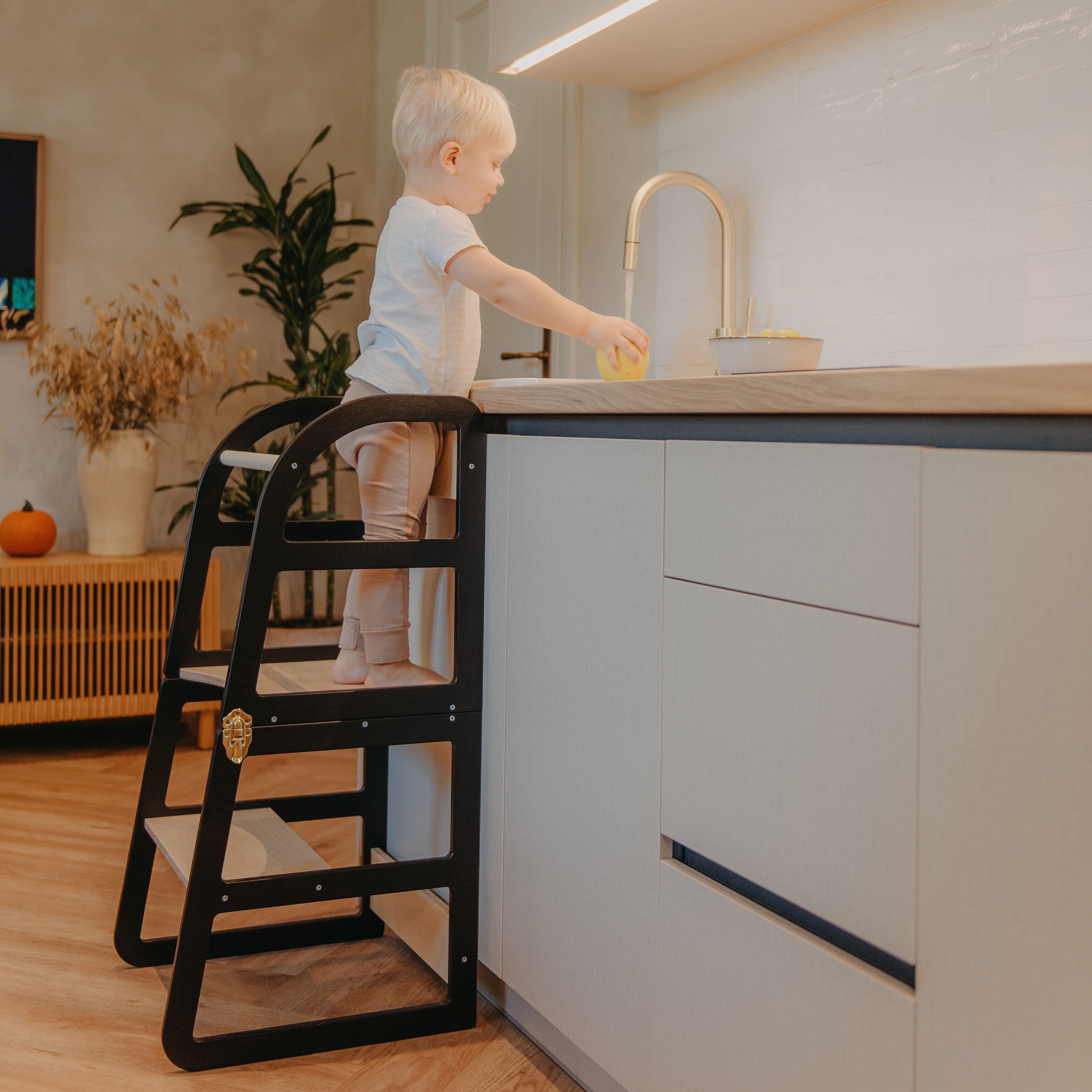 Child standing on a black transformable kitchen tower to independently reach the kitchen sink