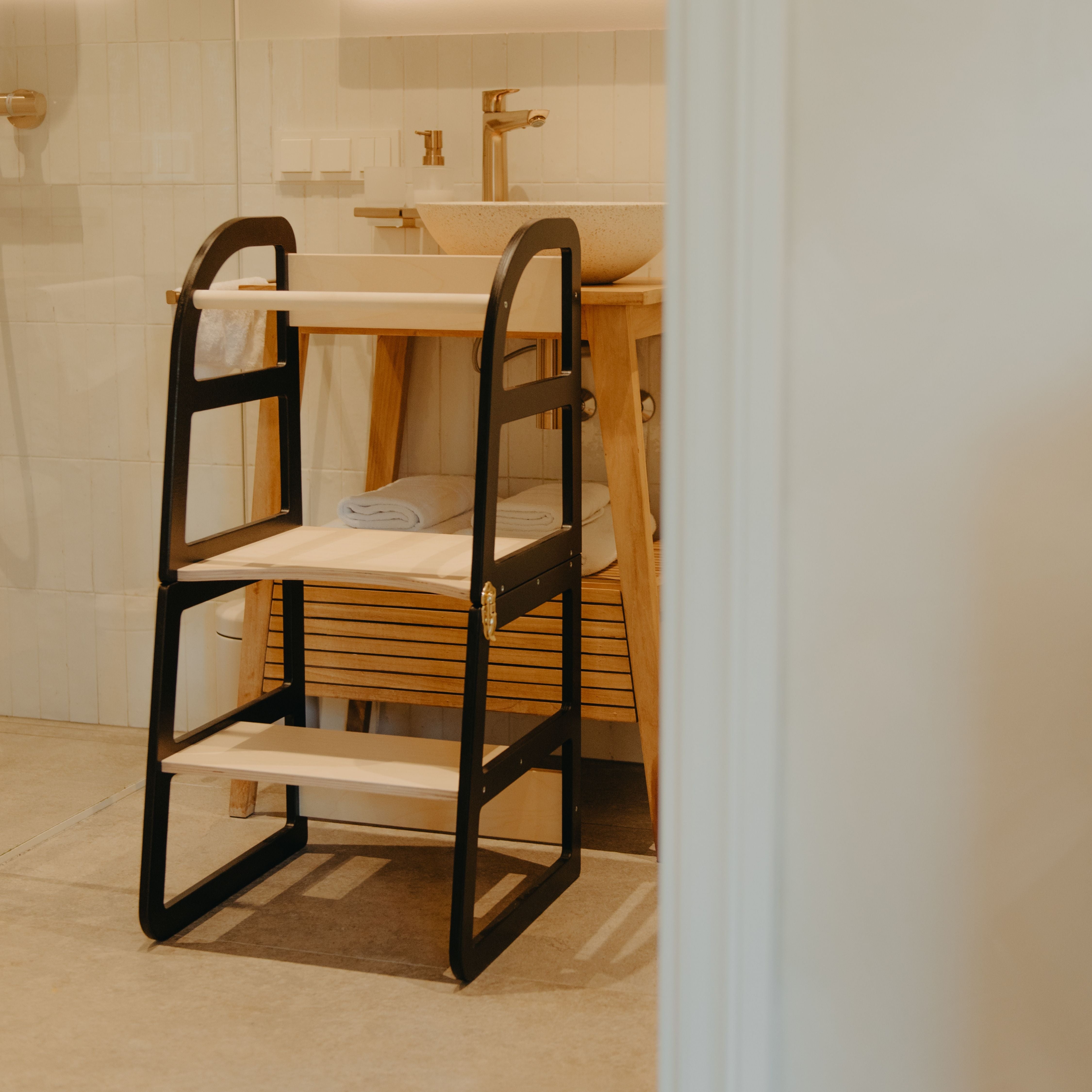 Black transformable kitchen tower positioned in a bathroom for children to reach the sink