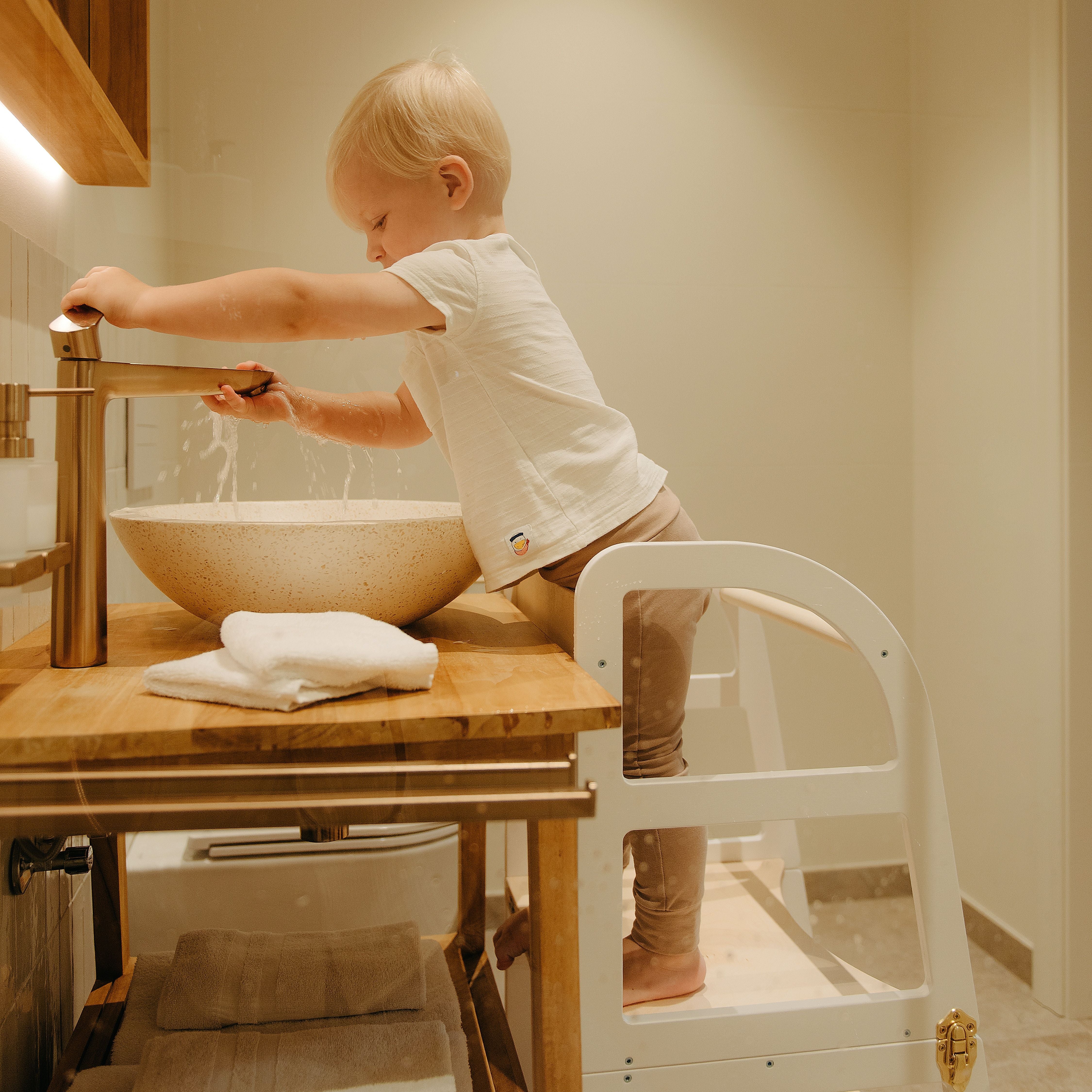 Toddler standing on a transformable kitchen tower to reach the bathroom sink and wash hands