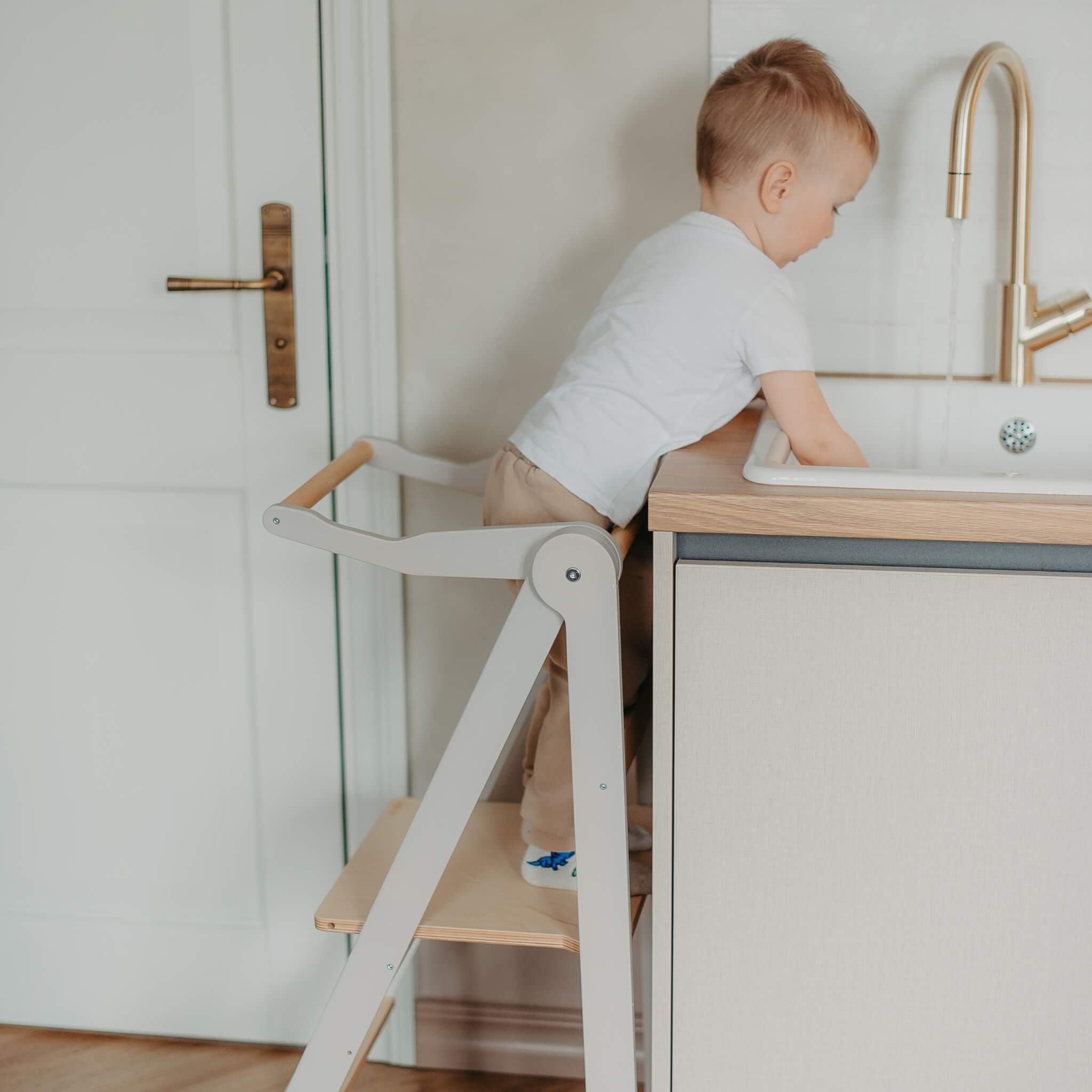 Child reaching kitchen countertop safely using wooden helper tower