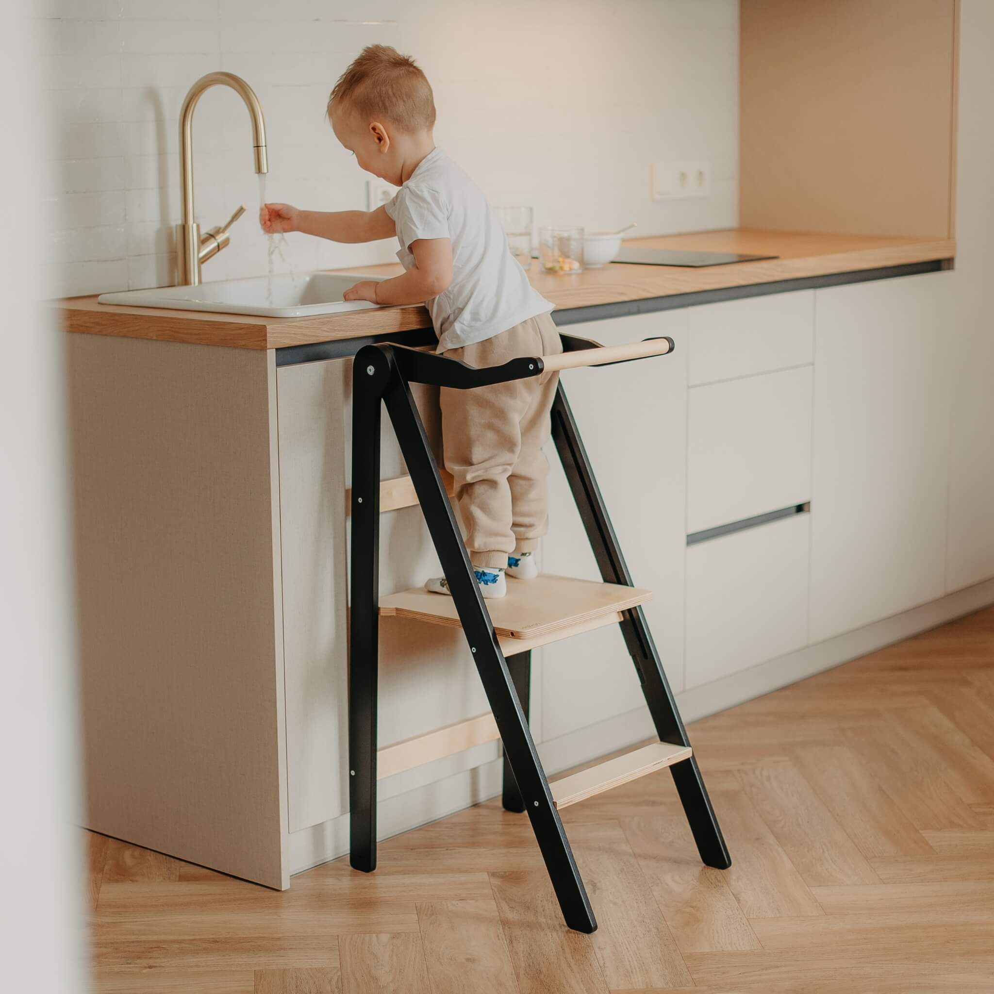 Child using wooden kitchen helper tower to reach countertop safely