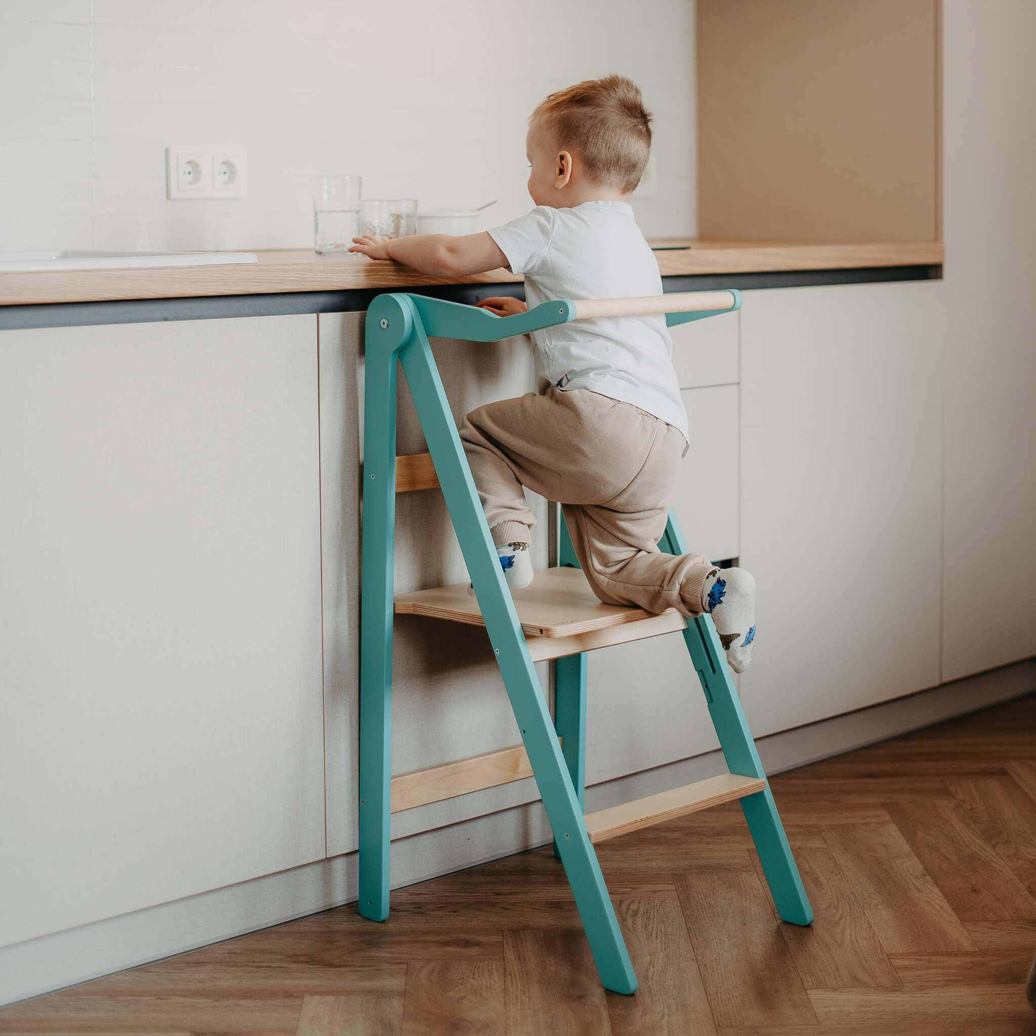 Child using foldable learning tower during kitchen activity at countertop