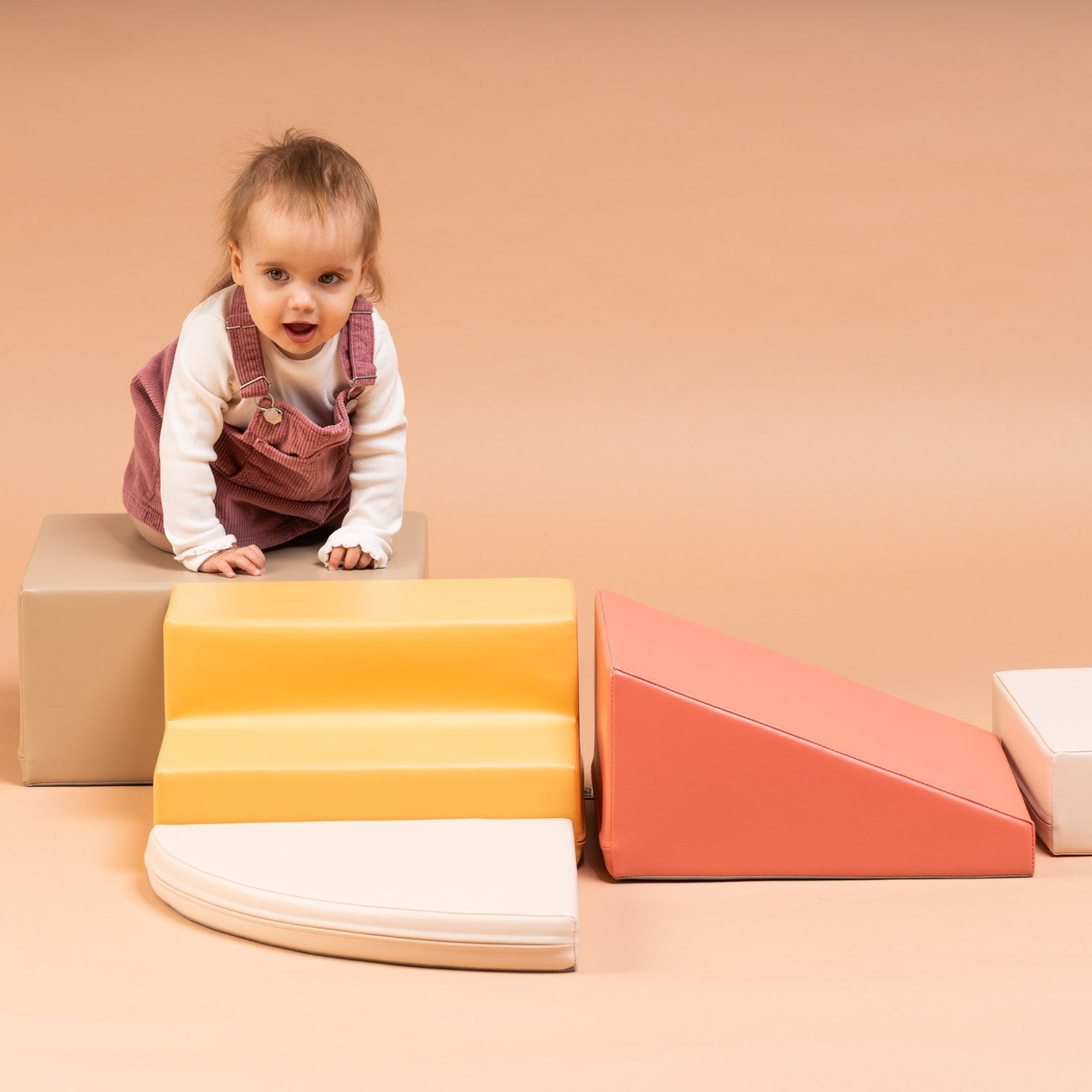 Toddler playing on soft play corner climber blocks in beige and pink tones