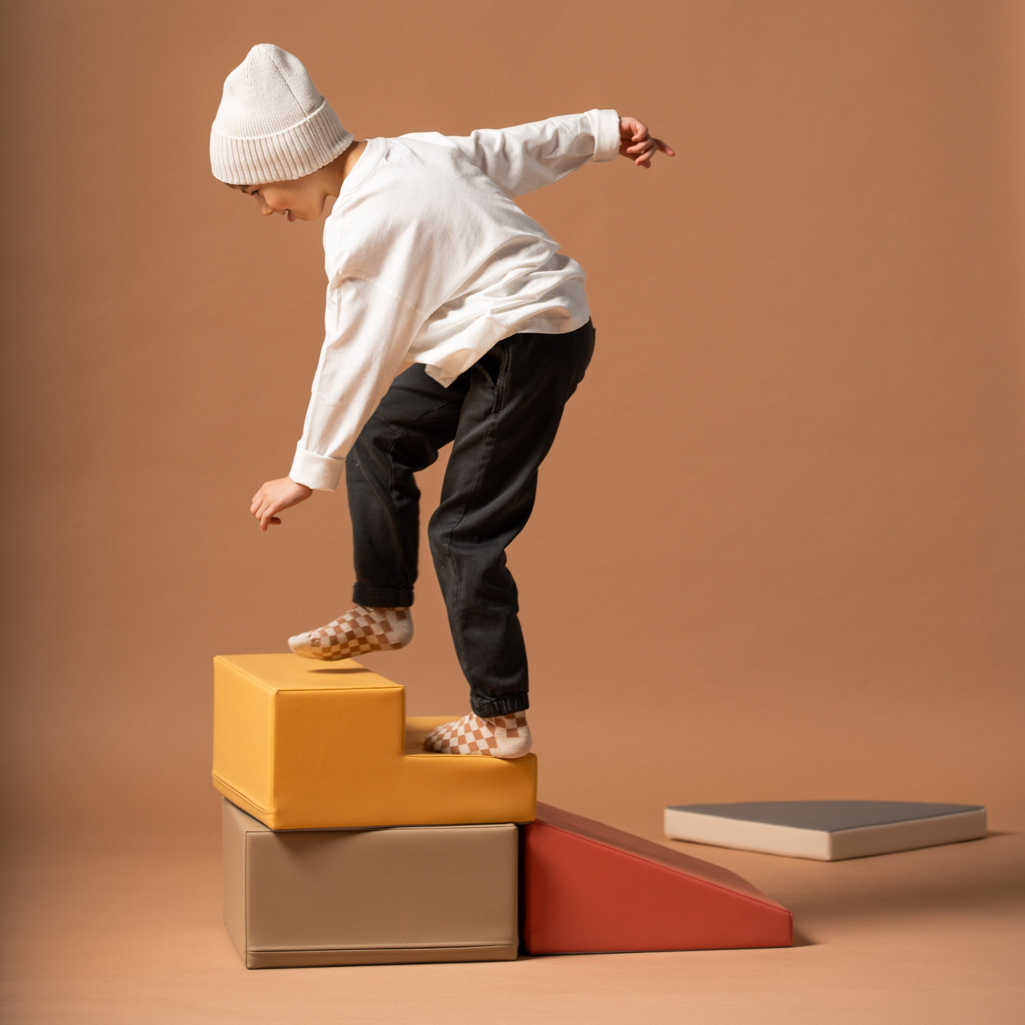 Child climbing and balancing on a soft play corner climber set in beige and pink