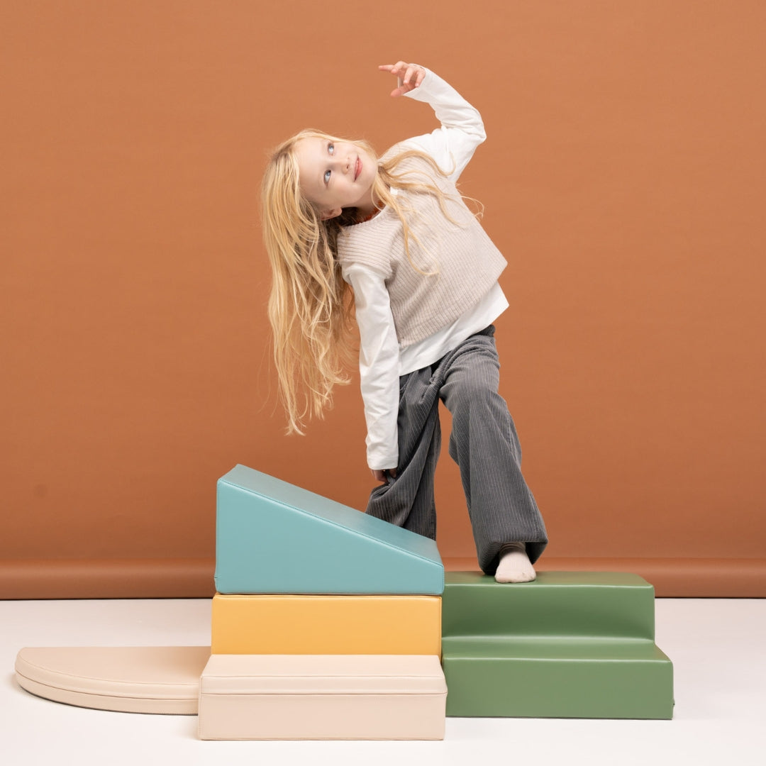 Toddler girl interacting with beige and turquoise soft foam climbing blocks in a corner play setup